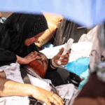 Seorang perempuan menggunakan kipas bertenaga baterai untuk mendinginkan seorang pria dalam ritual lempar jumrah. Gambar: BBC